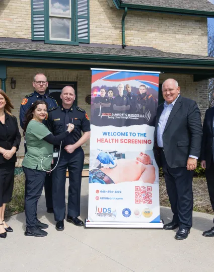 City staff and fire chiefs standing beside a "Welcome to the Health Screening" sign.
